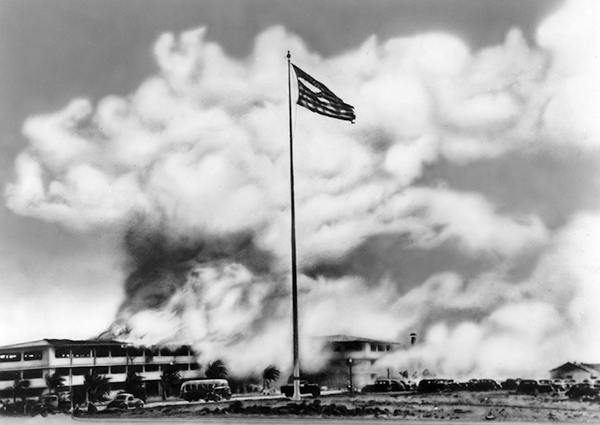 This iconic photo shows Hickam's brand-new barracks in flames after the Japanese attack. The truck at the base of the flag pole belongs to Herb’s company, members of which were fixing a damaged cable. The tattered flag in the photo later flew above the United Nations charter meeting in San Francisco, over the Big Three conference at Potsdam, and above the White House on August 14, 1945, when the Japanese surrendered. (Signal Corps photo from Herb’s collection)